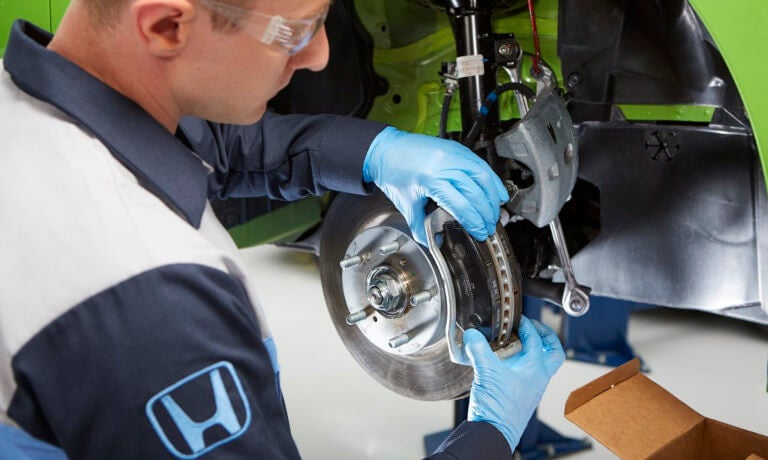 Honda mechanic replacing brake pads on a car